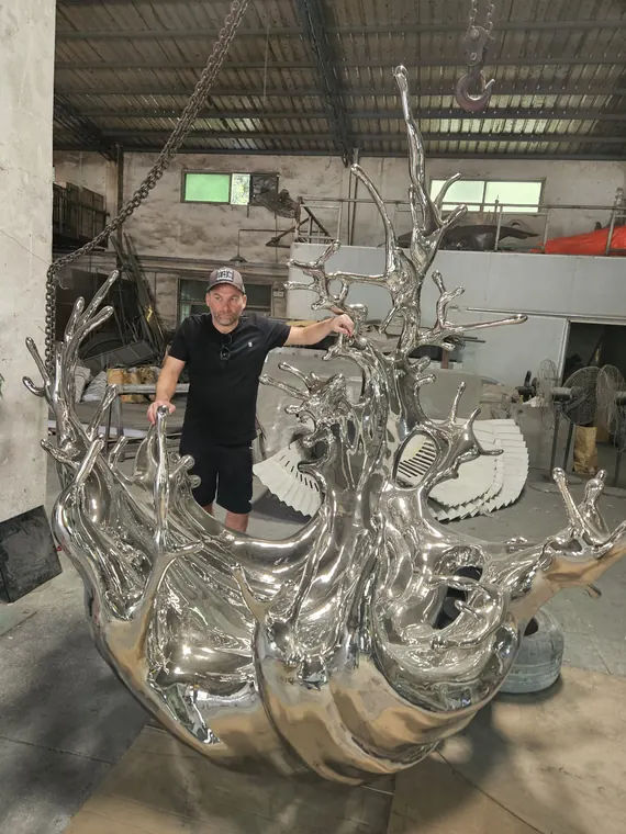 Dan Pearce with a large polished steel splash sculpture in the foundry